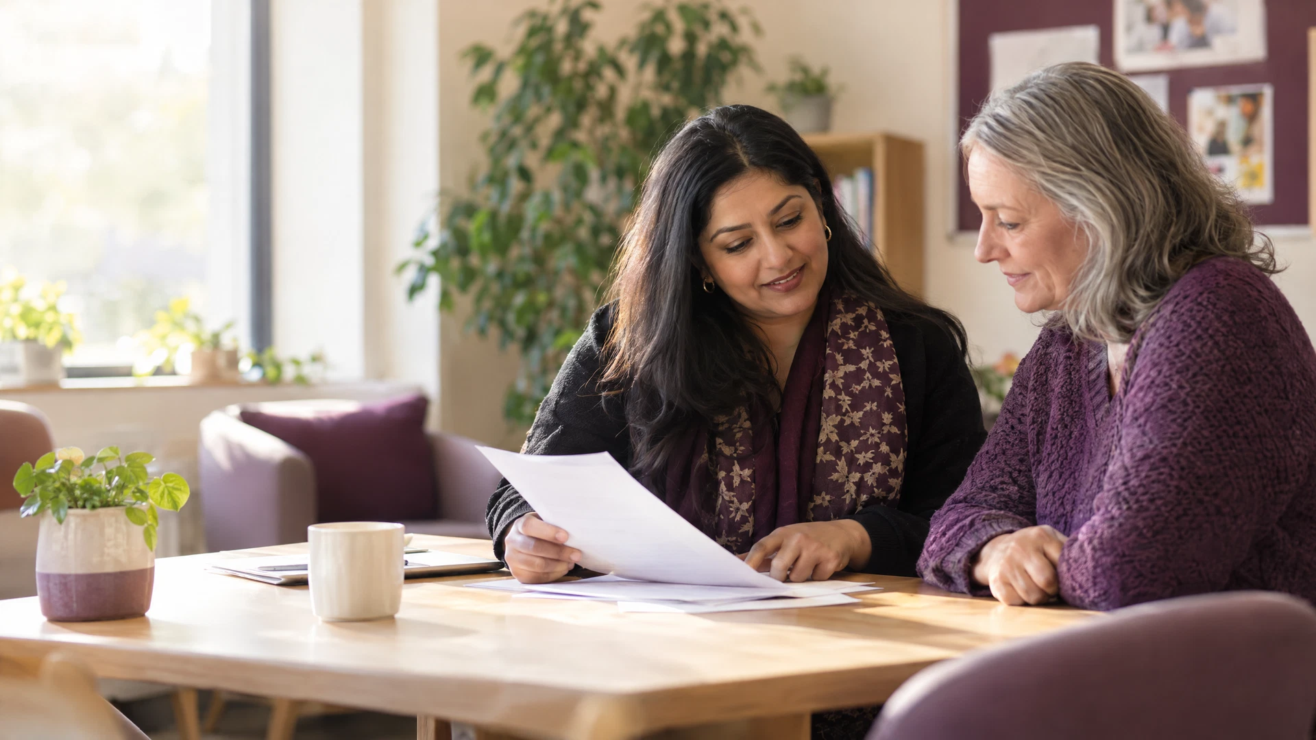 Two adults having a calm, supportive conversation about paperwork in a warm community space.